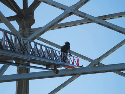 (4) The tip of the ladder is placed just above the top plate of a horizontal truss. A firefighter climbs to the tip to check the accuracy of the ladder placement. Note that the ladder is not touching the bridge.