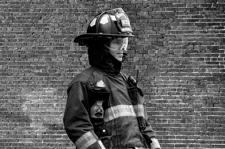 At sunset the firefighter appears much darker than the brick wall behind him.
