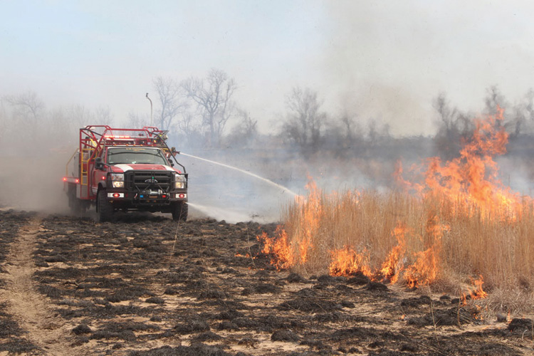 A Type 6 wildland engine built by Blanchat Manufacturing Inc. uses its bumper turret and attack position handline to fight a prairie fire from the black.