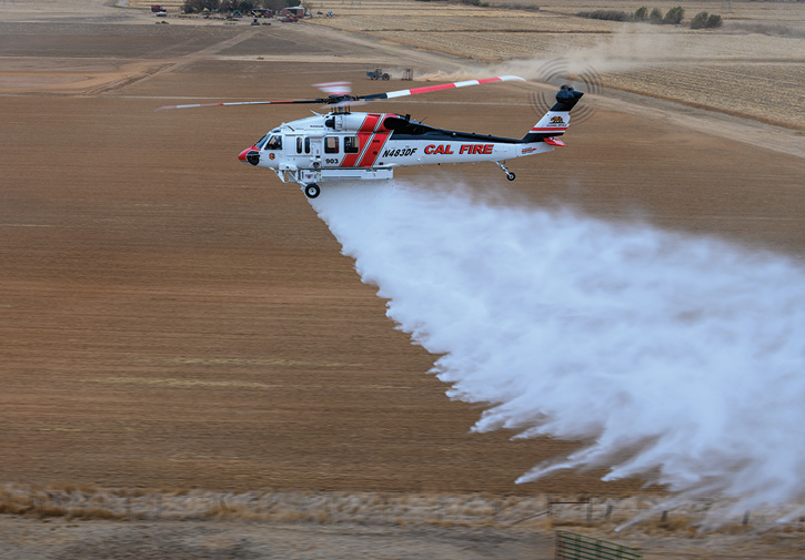 This CAL FIRE UH-1H Bell helicopter is dropping water out of its 320-gallon tank.