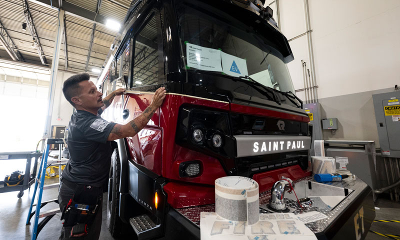 Adam Brinkman, with Grafix Shoppe, applies trim decals on to a Rosenbauer RTX engine for the St. Paul Fire Department at Rosenbauer’s manufacturing facility in Wyoming, Minnesota, on Wednesday, Aug 7, 2024. St. Paul’s newest engine will be Minnesota’s first electric rig and is scheduled to go into service in late September. (John Autey / Pioneer Press)